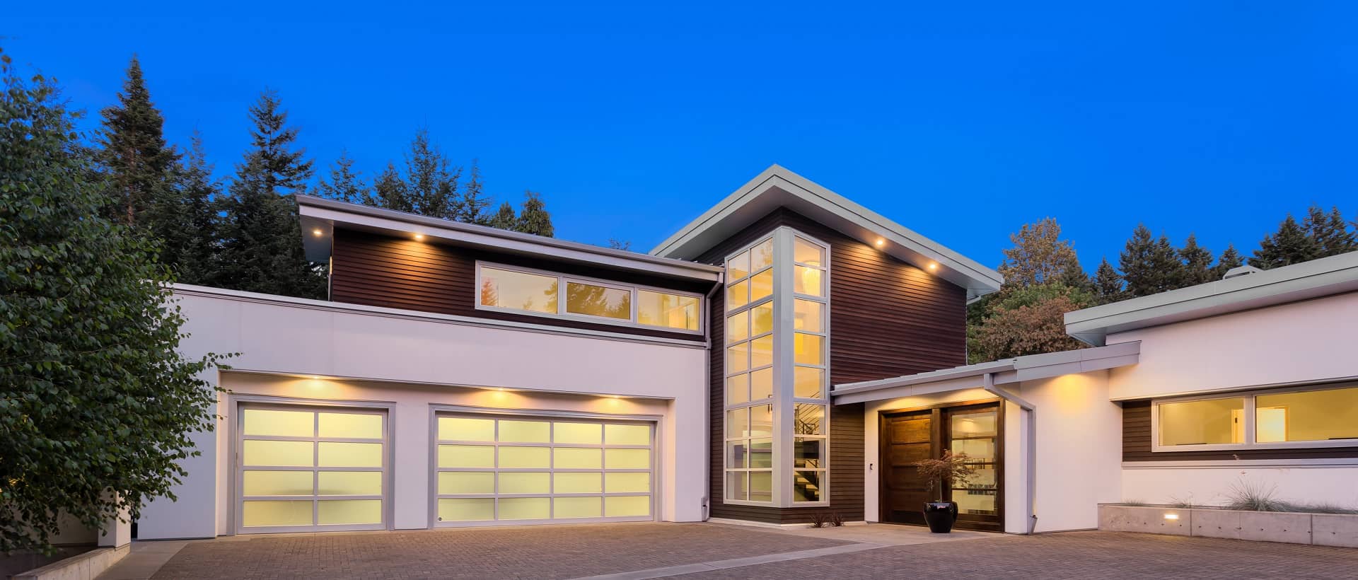 Facade of large, luxury home with expansive driveway with colorful sunset backdrop